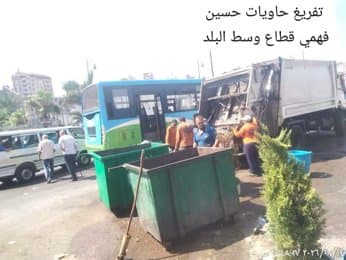 عمال يفرغون حاويات القمامة في سيارة النظافة
