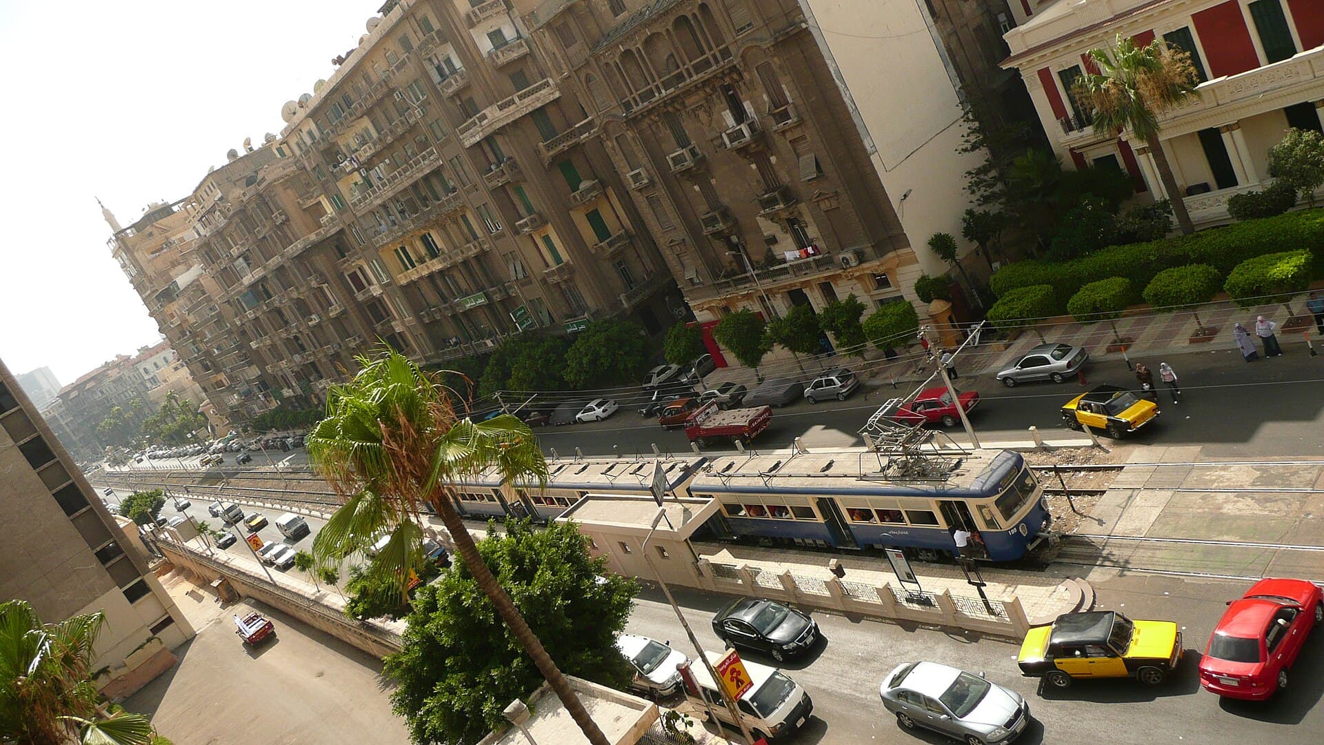 ترام أزرق يسير في شارع بوسط الإسكندرية بين حركة السيارات
