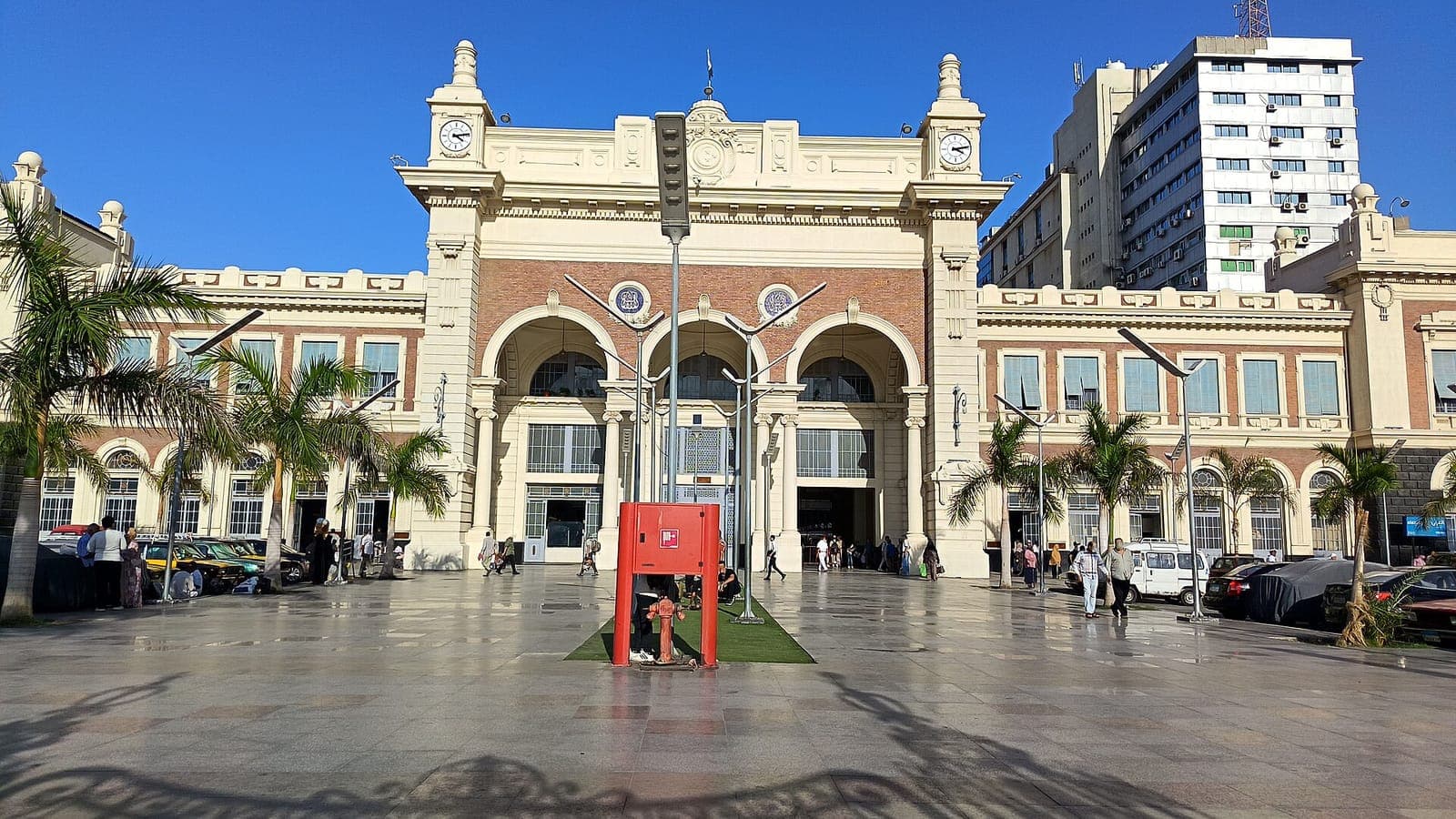 الواجهة الرئيسية لمحطة مصر للسكك الحديدية بالإسكندرية بأقواسها وبرجي الساعة، مع الساحة الأمامية في وضح النهار.